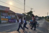 Anggota Polsek Pugung Polres Tanggamus saat menyebrangkan pelajar, Selasa 3 September 2024.