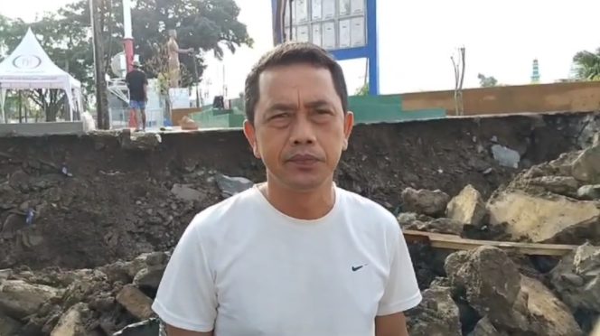 
 Tokoh Pemuda Kota Agung, Taufik Abah Salam saat memberikan komentar dengan latar belakang TPT Proyek RTH Ir. Soekarno yang ambrol, Sabtu 11 Januari 2025 | Herdi/Media Prioritastv.com.