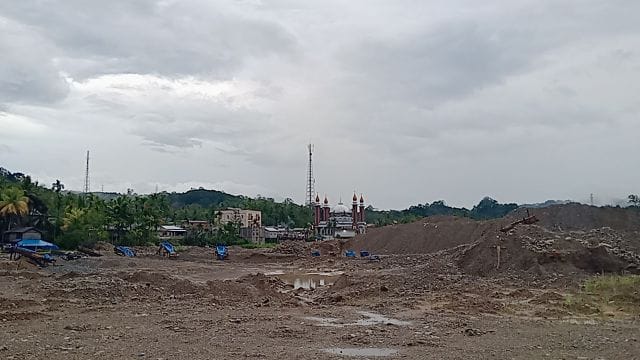 Lahan bekas aktivitas tambang emas ilegal di Mandailing Natal, terlihat tergenang dan dikelilingi gundukan tanah, dengan latar belakang pemukiman warga dan masjid yang berdiri tak jauh dari lokasi. (Putra/Prioritastv.com)