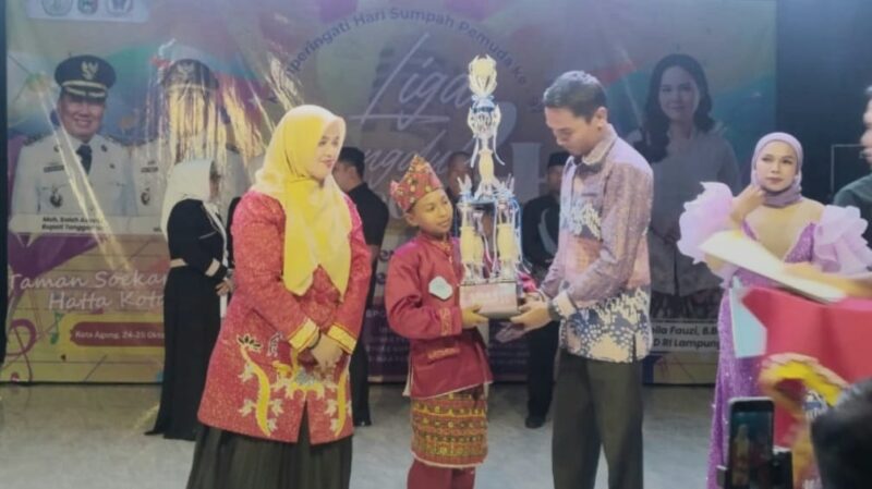 Wabup Tanggamus Agus Suranto saat menyerahkan hadiah kepada Hikmatul Fadilah, pelajar kelas 5 SD asal Pekon Tengor, Kecamatan Cukuh Balak yang berhasil meraih Juara 1 Liga Dangdut 4 Tanggamus 2025 STEBI Tanggamus bekerja sama dengan AWPI Tanggamus berlangsung meriah di Taman Soekarno, Kota Agung, Sabtu malam (25/10/2025) | Herdi/Media Prioritastv.com.