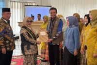 Bunda Literasi Tanggamus Hj. Siti Mahmudah saat menyerahkan surat pengukuhan Penggerak dan Duta Literasi dan Duta Baca Kabupaten kepada Wabup Agus Suranto di GSG Islamic Center Kota Agung, Kamis 4 Desember 2025 | Herdi/Media Prioritastv.com.