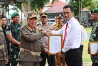 Bupati Tanggamus H. Moh. Saleh Asnawi saat menyerahkan piagam penghargaan kepada perwakilan Polres Tanggamus di Lapangan Merdeka, Kota Agung, Selasa 13 Januari 2026 | Herdi/Media Prioritastv.com.